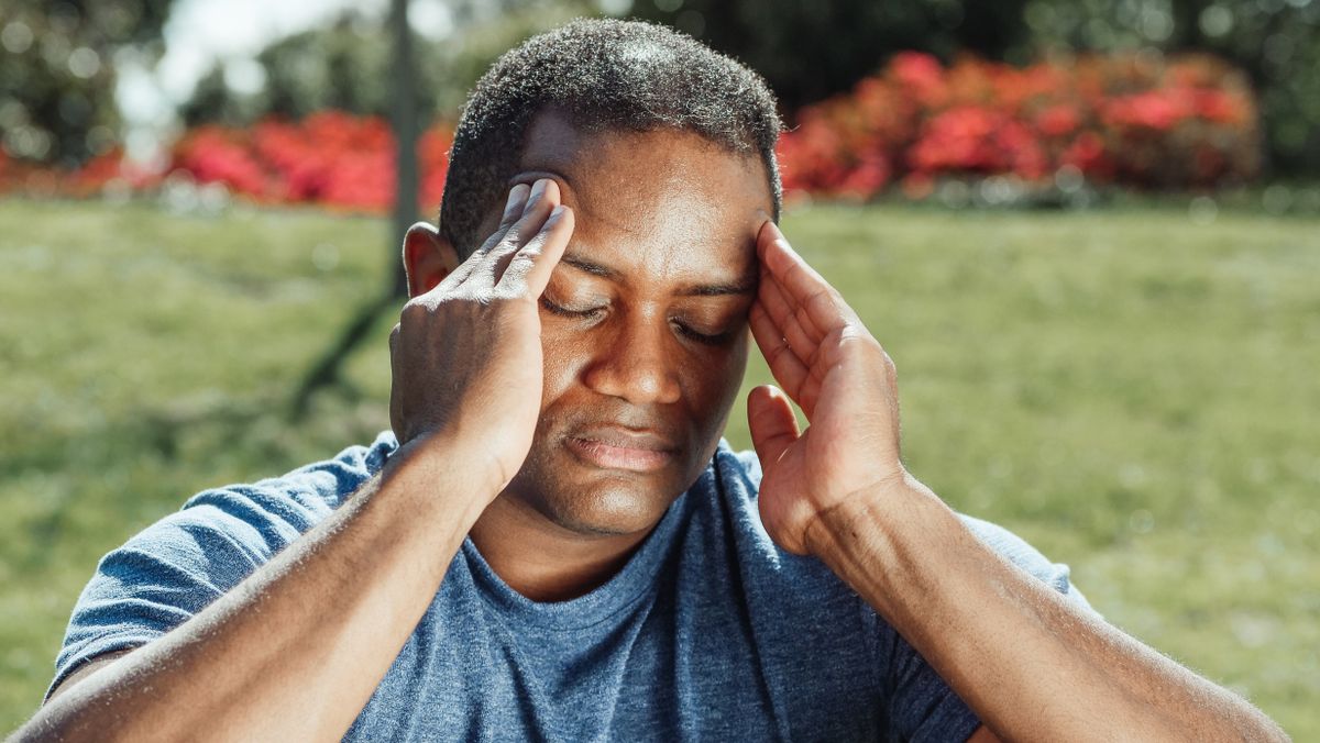 middle-aged person holding their knee in discomfort while sitting on a park bench