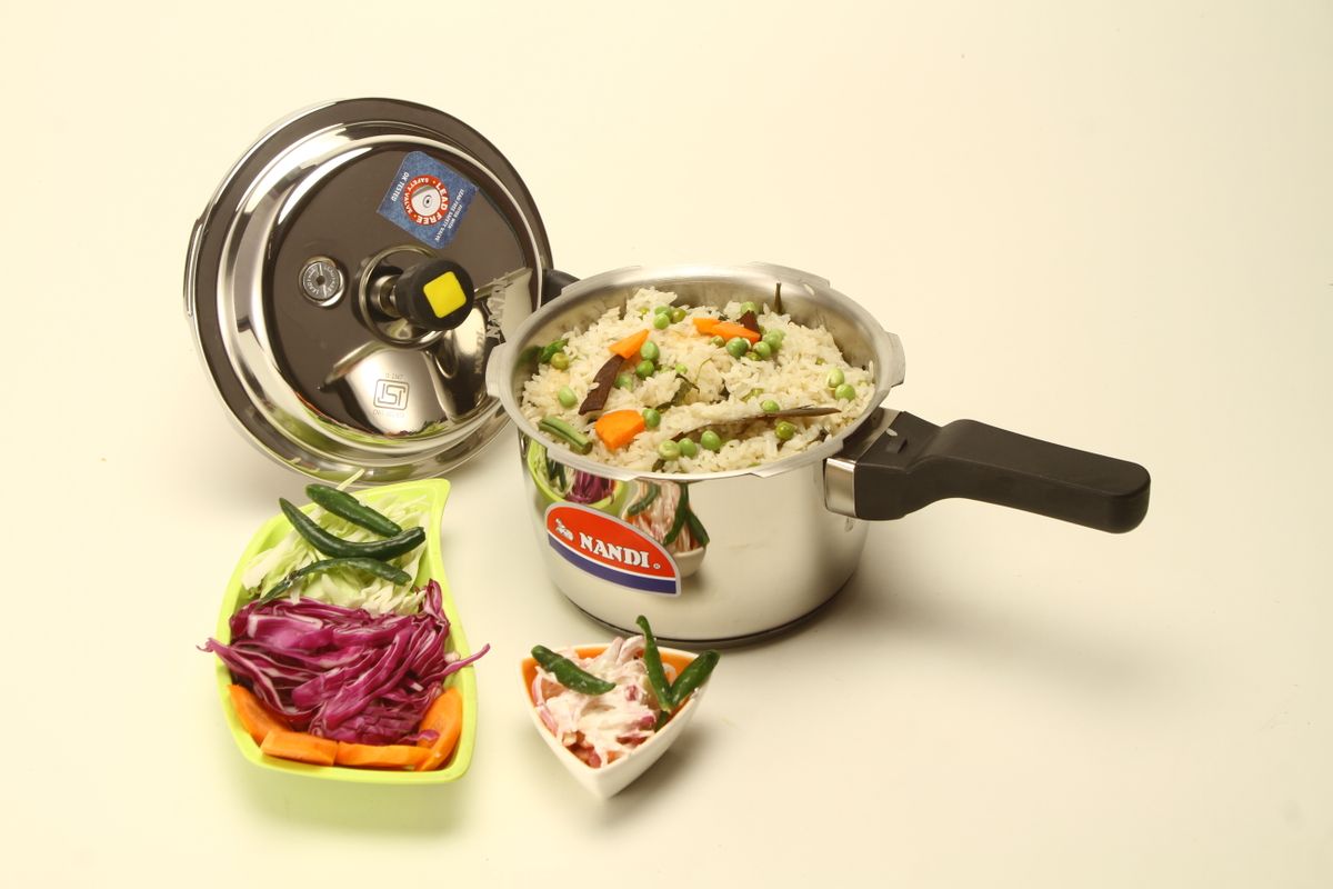 Stainless steel pressure cooker with cooked rice and vegetables, garnished with salads.