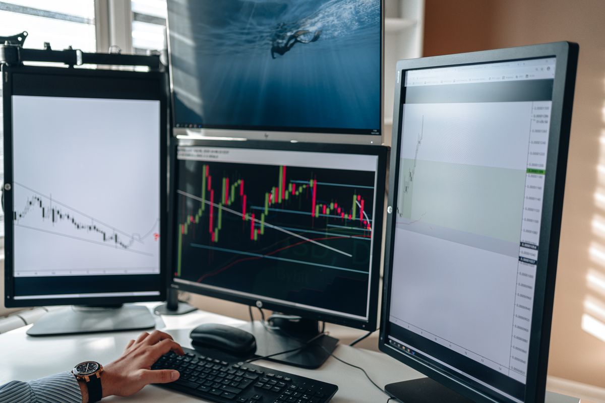 A close-up shot of a person intensely analyzing complex financial stock market charts on a high-end dual monitor setup.
