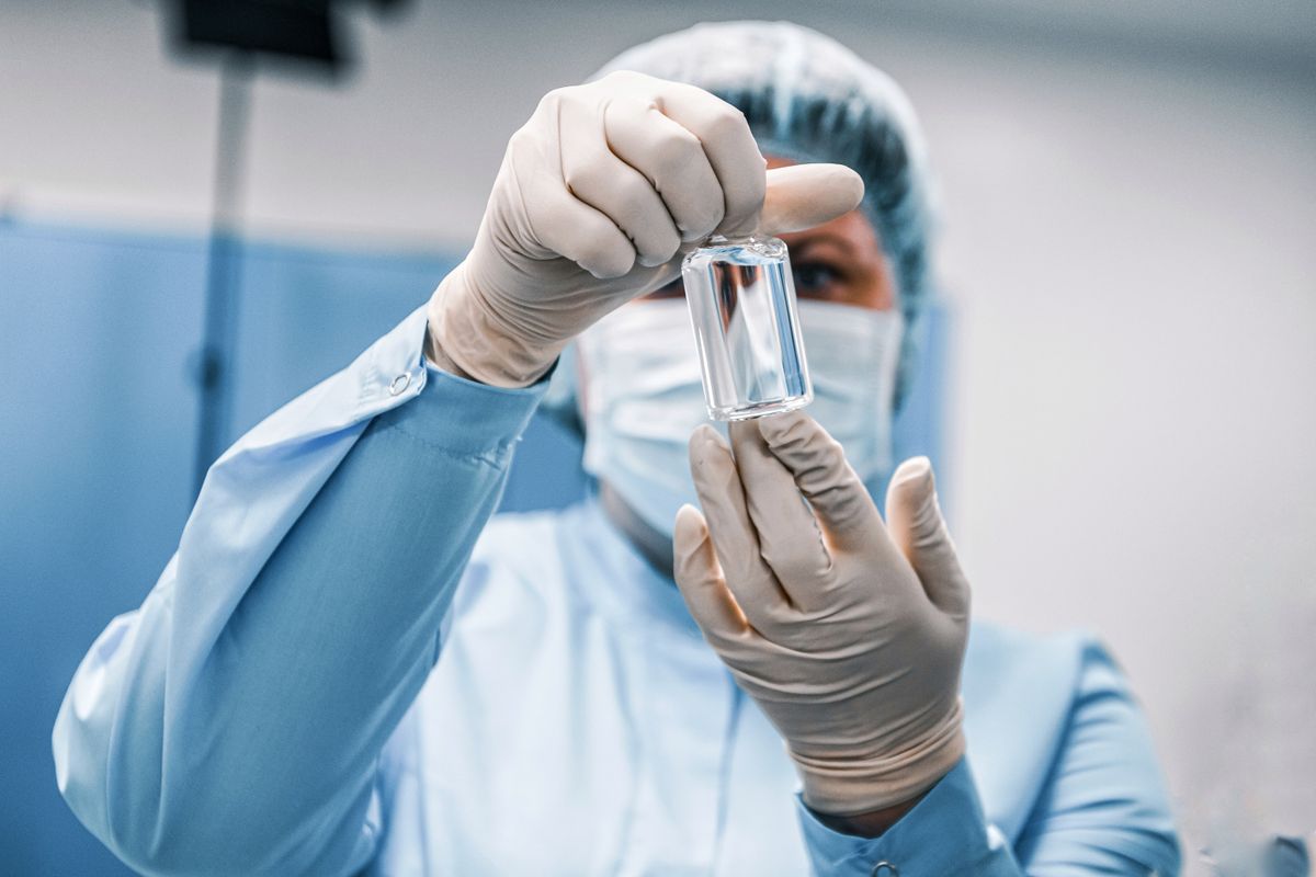 Close-up of a healthcare worker in protective gear examining a medical vial.
