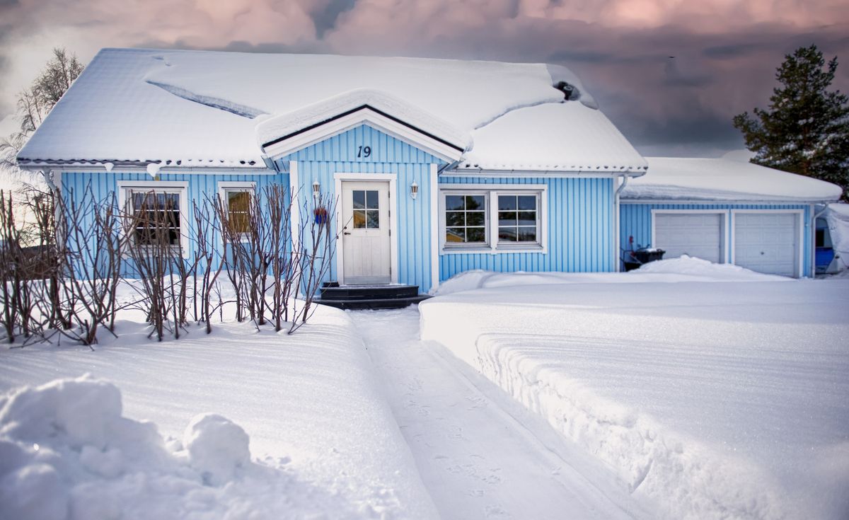 Blue house covered in snow during winter with a serene sky backdrop.